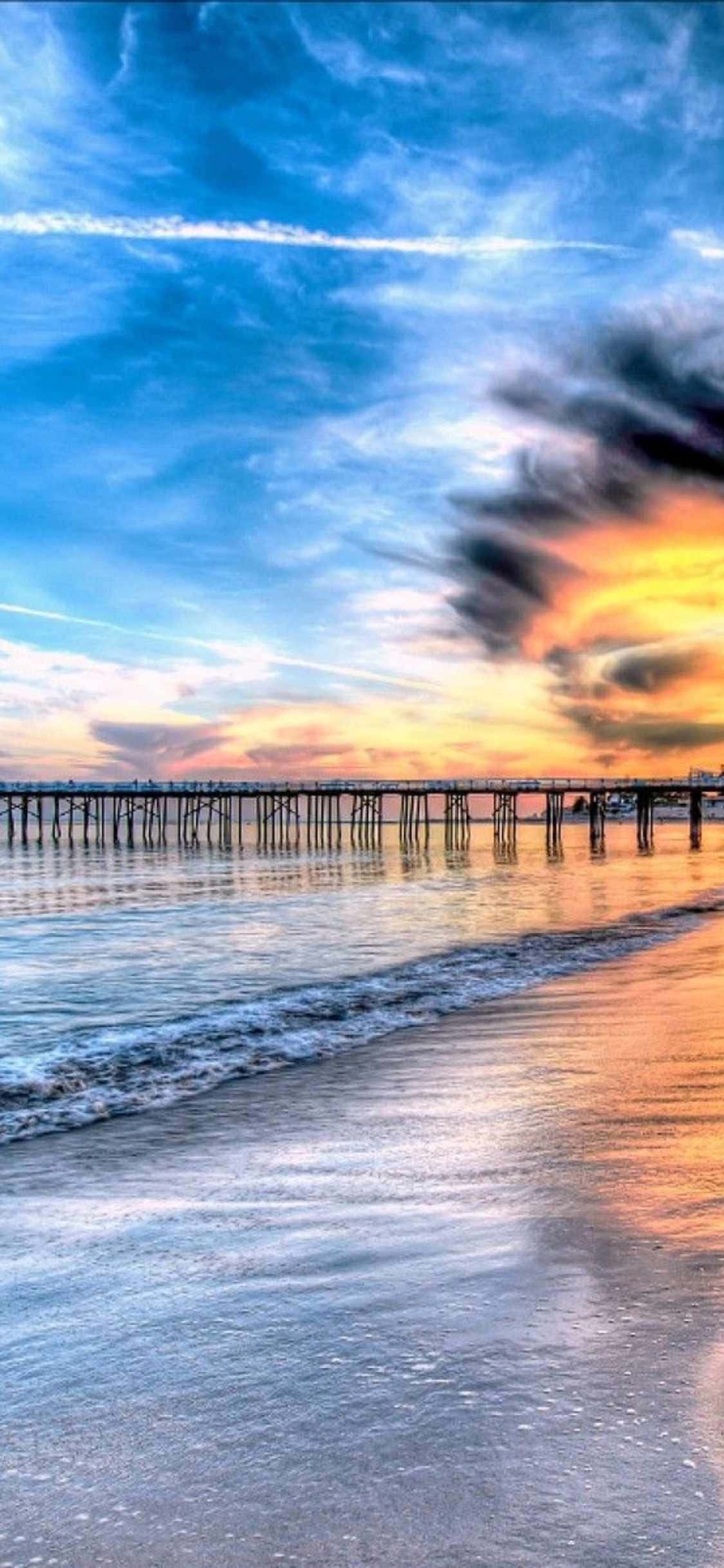 a pier with a sunset over the ocean วอลเปเปอร์