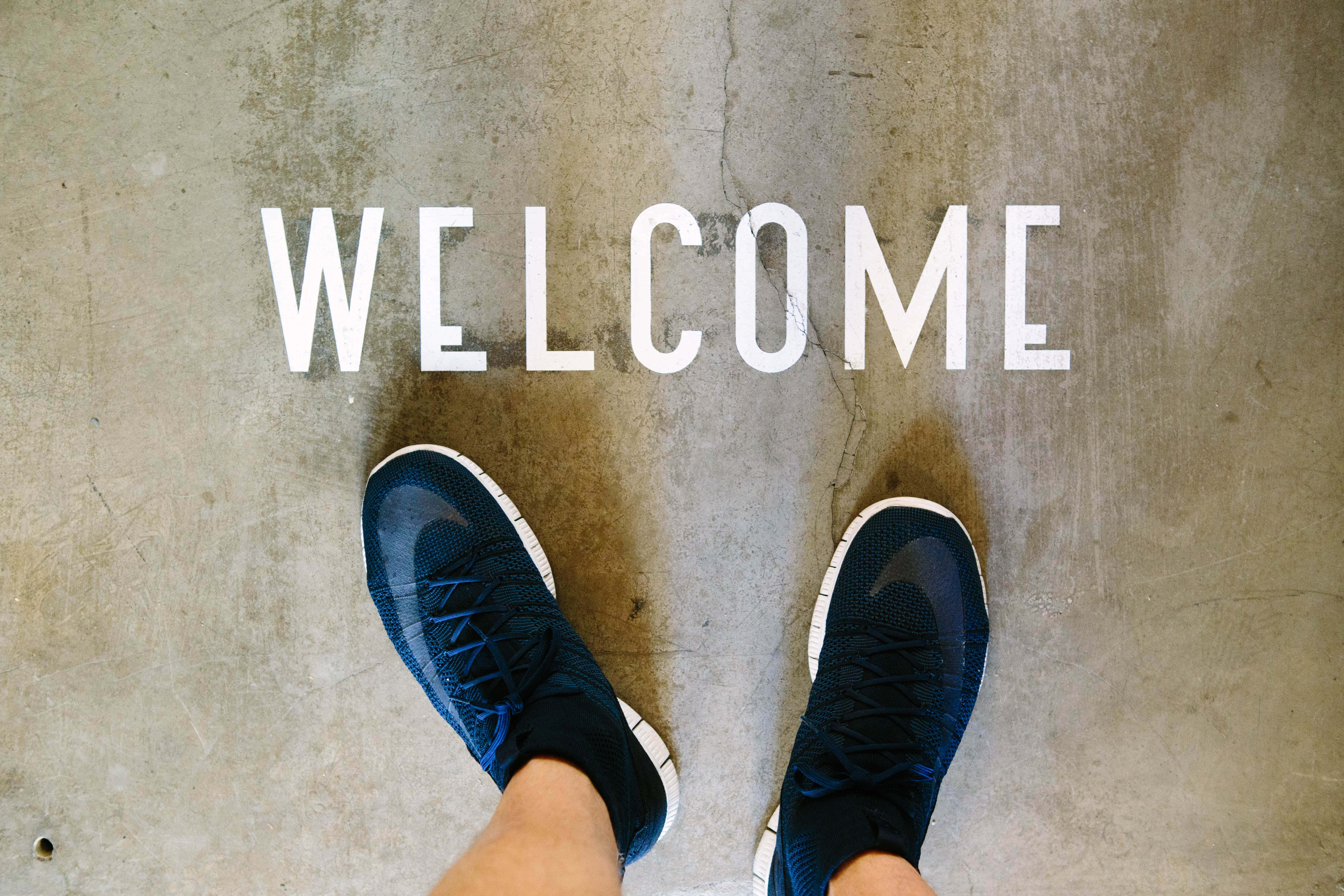 เท้าของคนยืนบนพื้นคอนกรีตที่มีคำว่า welcome วอลเปเปอร์