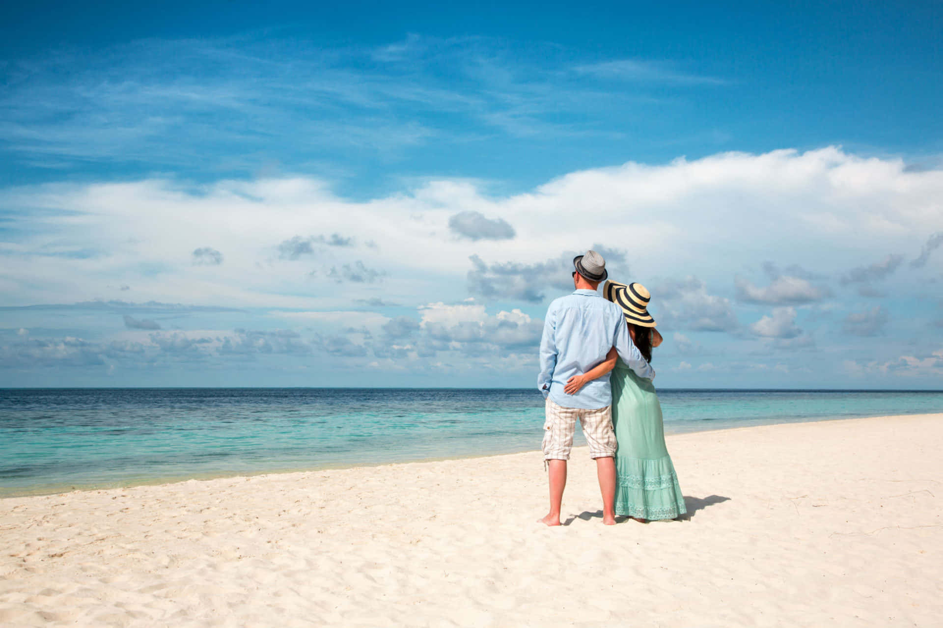 คู่รักยืนอยู่บนชายหาดใต้ท้องฟ้าสีคราม วอลเปเปอร์