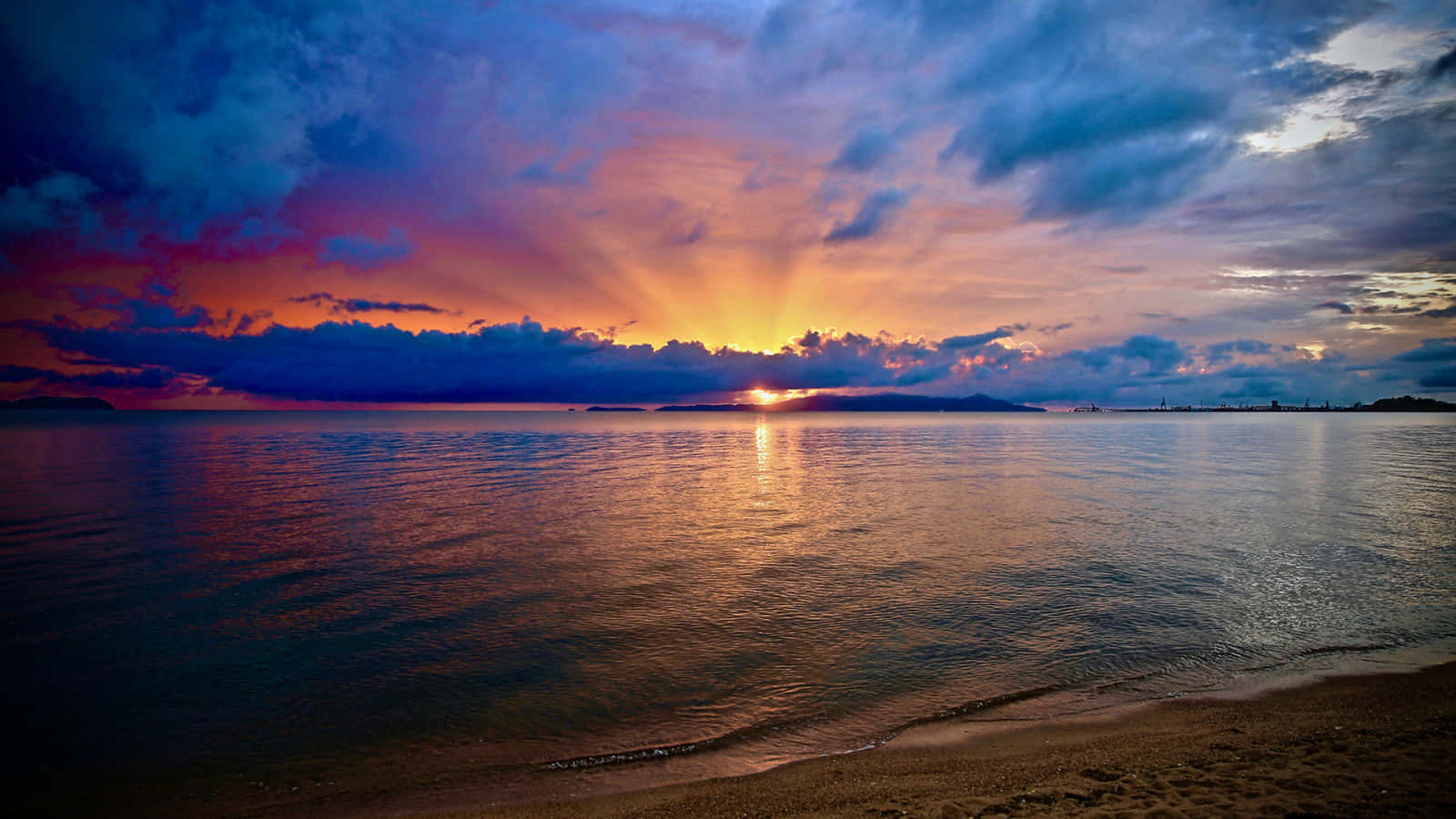 พระอาทิตย์ตกที่ชายหาดสวยงามเมื่อมองจากระยะไกล วอลเปเปอร์