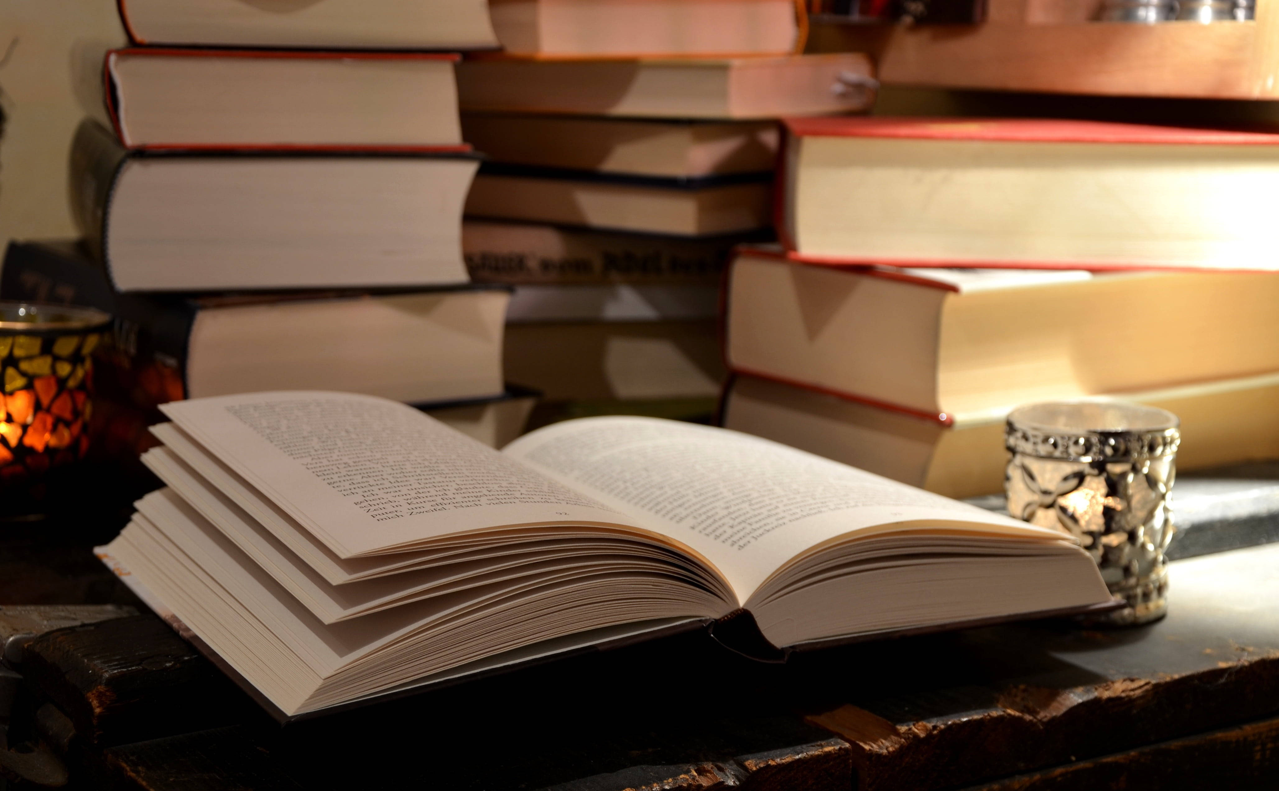 ภาพหนังสือเปิดบนโต๊ะ รายล้อมด้วยหนังสืออ้างอิงเล่มอื่นๆ วอลเปเปอร์