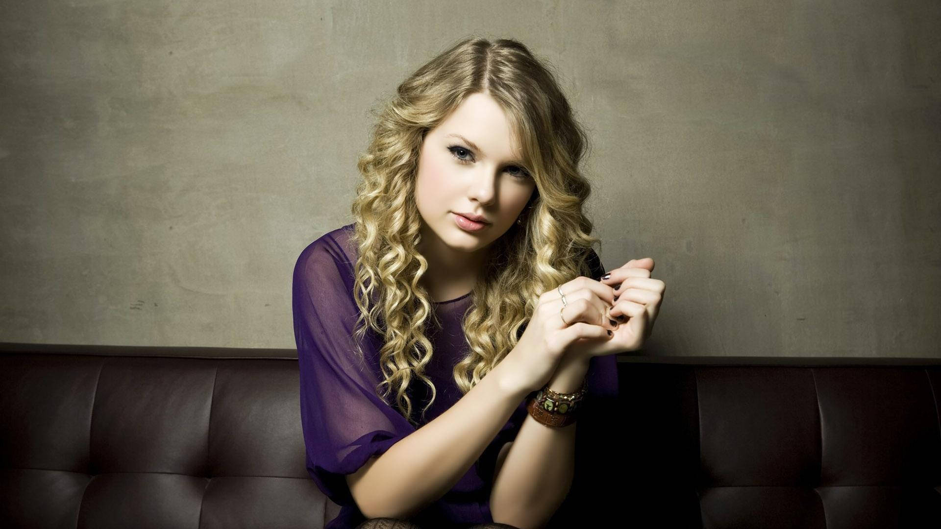 วอลเปเปอร์เทย์เลอร์ สวิฟต์ ผมลอนนั่งสวมเสื้อตาข่ายสีม่วง — Taylor Swift วอลเปเปอร์