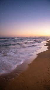 ภาพชายหาดสงบยามพลบค่ำ ท้องฟีาสีพาสเทลและคลื่นอ่อนโยน วอลเปเปอร์ที่ให้ความรู้สึกสงบ