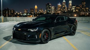 รถคามาโร ZL1 สีดำจอดอยู่บนลานจอดรถบนดาดฟ้า โดยมีเส้นขอบฟ้าของเมืองในยามค่ำคืน